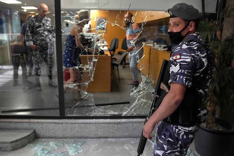 A Lebanese policeman stands guard next to a bank window broken by depositors who had demanded access to their money. An activist group said it will continue to organise bank raids to help people retrieve their trapped savings.  AP photo