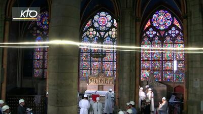 With the fine windows above the first Mass is celebrated in a side chapel, two months after a devastating fire engulfed the Notre-Dame de Paris cathedral, Saturday June 15, 2019, in Paris.  Michel Aupetit, Archbishop of Paris, wore a hard-hat helmet, burnt wood debris was still visible and only about 30 people were let inside, but Notre Dame Cathedral on Saturday held its first Mass since the devastating April 15 fire that ravaged its roof and toppled its masterpiece spire. (KTO via AP)