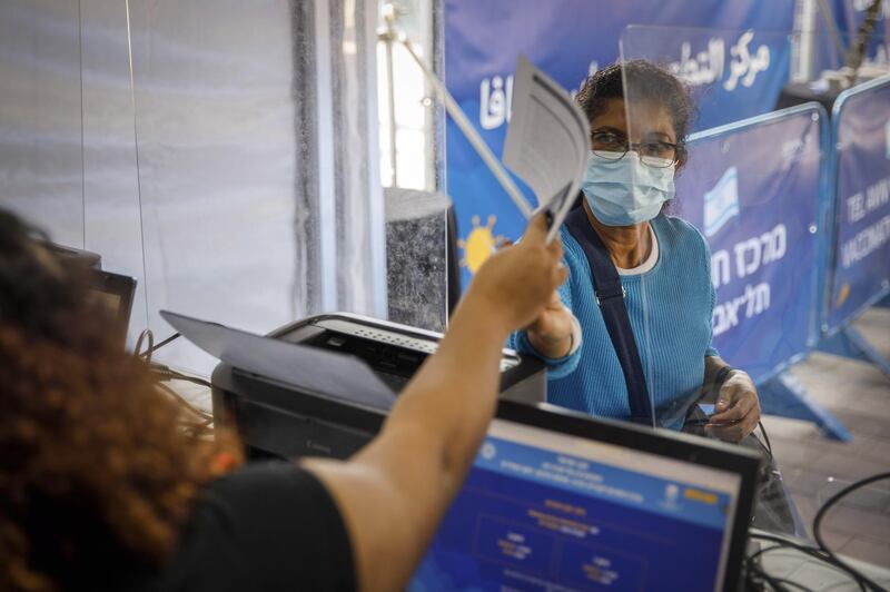 A foreign national hands over a document and passport at a registration desk at a vaccination centre in Tel Aviv. Bloomberg