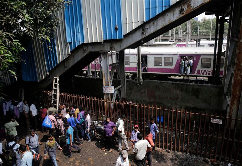 Commuters stand under a pedestrian bridge where a stampede took place at the Elphinstone local station, in Mumbai, India, Friday, Sept. 29, 2017. The stampede broke out on a crowded pedestrian bridge connecting two railway stations in Mumbai during the Friday morning rush killing a number of people, police said. (AP Photo/Rafiq Maqbool)