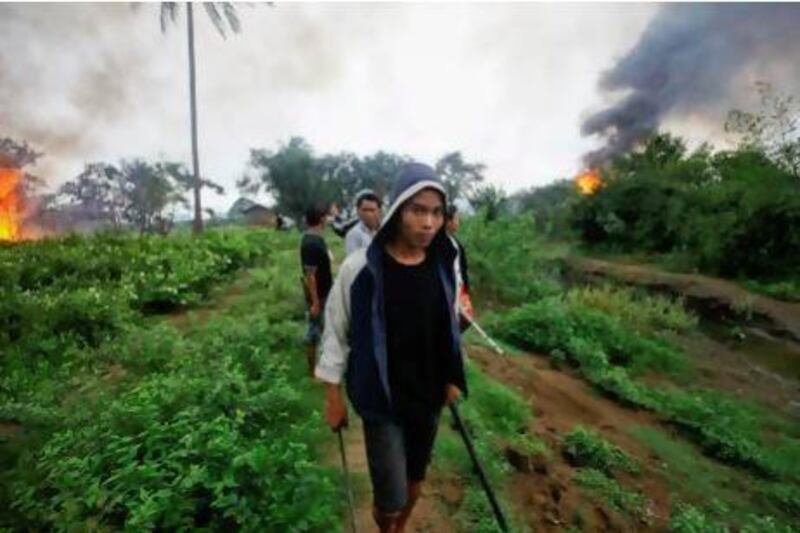 RNPS IMAGES OF THE YEAR 2012 - An Ethnic Rakhine man holds homemade weapons as he walks in front of houses that were burnt during fighting between Buddhist Rakhine and Muslim Rohingya communities in Sittwe June 10, 2012. Northwest Myanmar was tense on Monday after sectarian violence engulfed its largest city at the weekend, with Reuters witnessing rival mobs of Muslims and Buddhists torching houses and police firing into the air to disperse crowds. REUTERS/Staff (MYANMAR - Tags: CIVIL UNREST RELIGION TPX IMAGES OF THE DAY) *** Local Caption *** POY230_POY-_1203_11.JPG