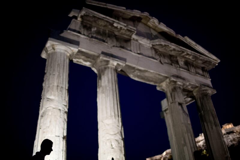 A man walks in front of the Gate of the ancient Roman agora with the ancient Acropolis hill seen in the background in Plaka district of Athens, Thursday, July 20, 2017. Greece says it is still waiting for the "right moment" to re-enter the bond market, playing down expectations of an issue by the end of the week. (AP Photo/Petros Giannakouris)