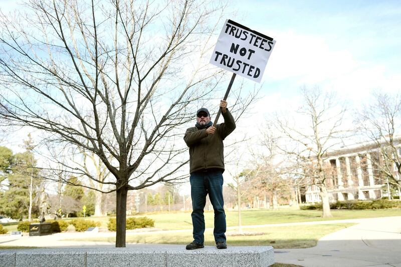 Bernie Trautmann holds a sign in protest of the Michigan State University Board of Trustees while it met on Friday, Jan. 26, 2018, outside the Hannah Administration Building on the MSU campus in East Lansing, Mich. Trautmann, an MSU grad, said he has a daughter currently enrolled and said in light of what's gone on during the Larry Nassar case, he has apprehension about sending another child to the university next year. The university's  athletic director announced his retirement Friday, becoming the second university official to step down this week over the school's handling of sexual abuse allegations against disgraced former sports doctor Nassar.  (Nick King /Lansing State Journal via AP)