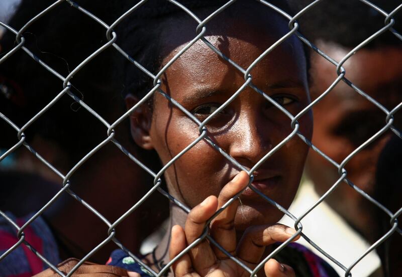 An Ethiopian refugee who fled fighting in the Tigray Region looks on from behind a fence as she waits with others at the Village 8 border reception center in Sudan's eastern Gedaref State. AFP