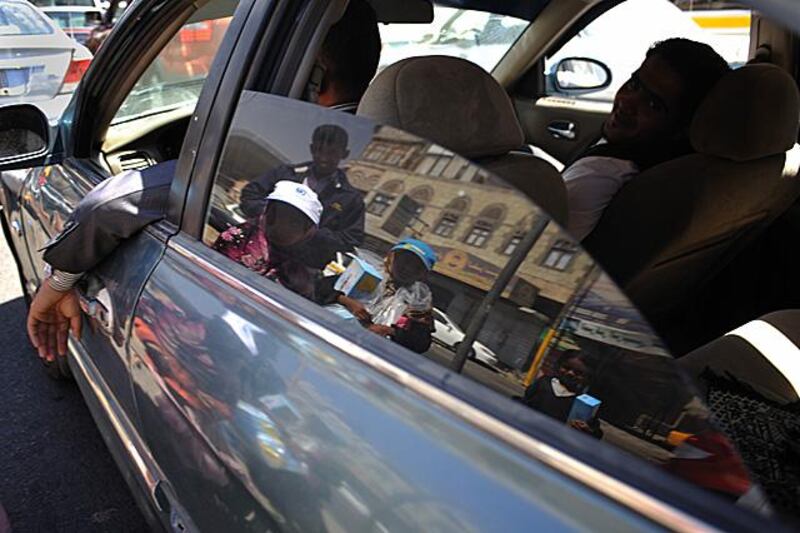 The reflection of three girls from the Hajiri family selling tissues to passing drivers at an intersection in downtown Sana'a. Photo: Lindsay Mackenzie for the National.