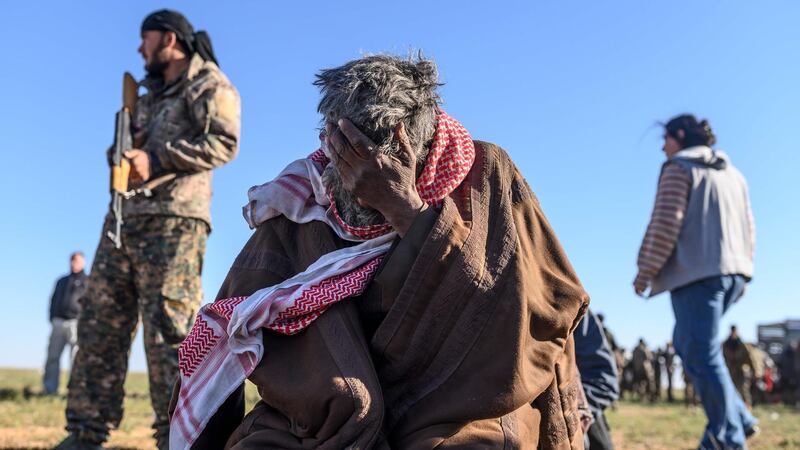 A member of the Kurdish-led Syrian Democratic Forces stands by as a man sits with his palm on his face, after leaving ISIS's klast stronghold of Baghouz, in the eastern Syrian Deir Ezzor province. AFP