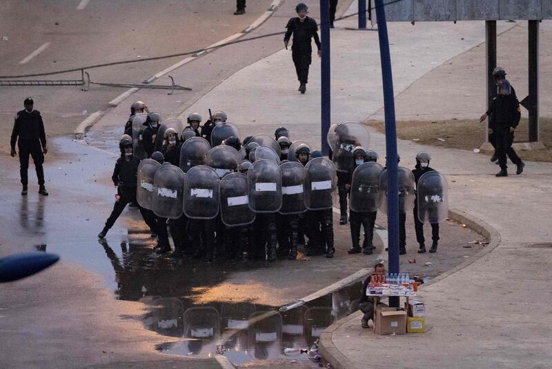 A street vendor hides behind his cigarette stand as Moroccan riot police draw up a formation behind him as they face migrants on the streets of Frideq unable to cross into the Spanish enclave of Ceuta. AFP