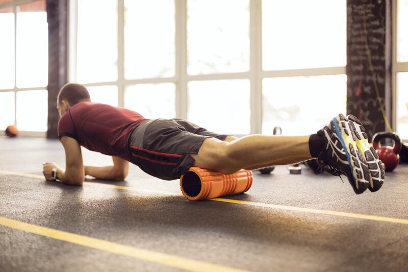 Young man athlete relaxing after training with kettle bells in the gym. He is practicing series of exercises witth foam roller