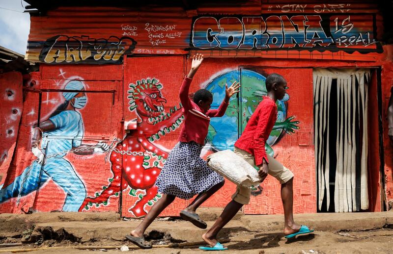 FILE - in this Wednesday, June 3, 2020 file photo, children run down a street past an informational mural warning people about the dangers of the new coronavirus, in the Kibera slum, or informal settlement, of Nairobi, Kenya. (AP Photo/Brian Inganga, File)