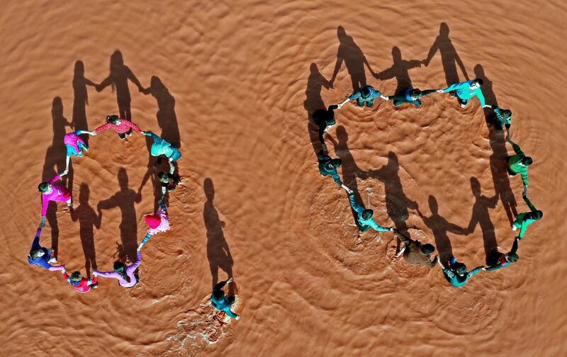 Children standing together holding hands in circles in a rainwater pond at the flooded Mukhayyam Al Khair camp near the village of Kafr Uruq in the north of Idlib province. AFP