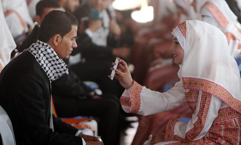 A Palestinian bride shows her groom a photo on her phone during the mass wedding ceremony funded by the President's Sheikh Khalifa bin Zayed Al Nahyan Foundation. Mahmud Hams / AFP