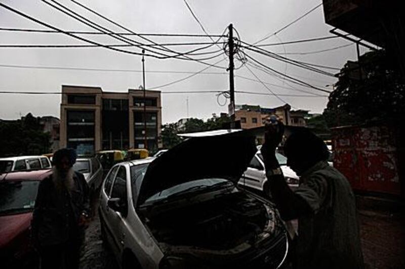 A mechanic repairs a car next to an electric pole which has illegal subsidiary wires attached to the main cables in New Delhi, India, during the power cut yesterday.