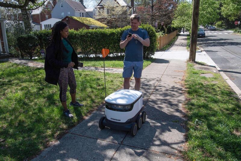 Kimmo Kartano uses his smartphone to open a food delivery robot from the Broad Branch Market grocery store as Audra Grant looks on in front of their house in the Chevy Chase neighborhood of Washington, DC, on April 9, 2020. - The store began using the robots about two weeks ago and makes 10-15 deliveries a day within a limited area of the neighborhood. (Photo by NICHOLAS KAMM / AFP)
