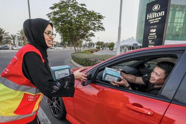 Volunteer Hana Al Braeki distributes food to motorists at the corner of 11th and 18th Street in Zayed Sports City. Victor Besa/The National Section