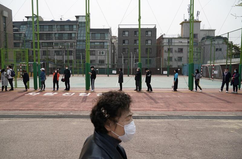 A woman walks past a queue of voters wearing masks while waiting to cast their ballots at a polling station in Seoul, South Korea. Reuters