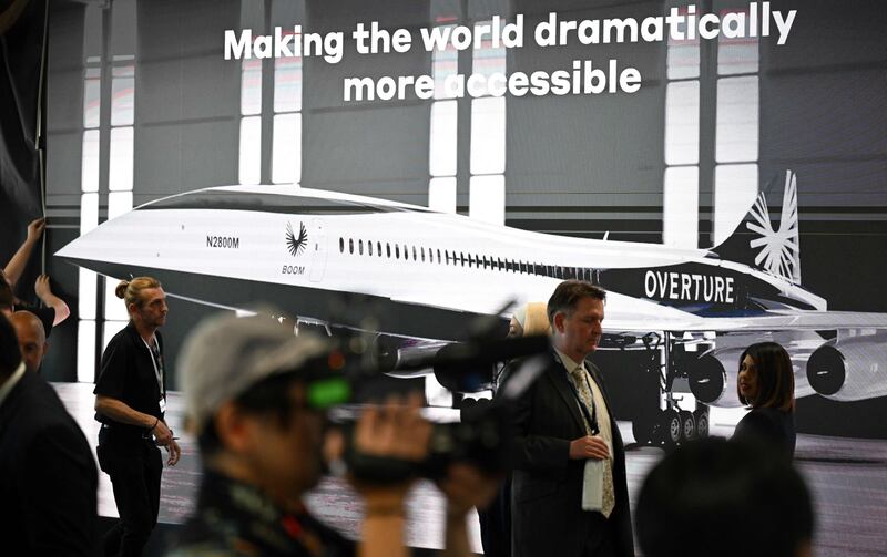 Attendees walk past a poster of a Boom Supersonic concept Overture aircraft. AFP