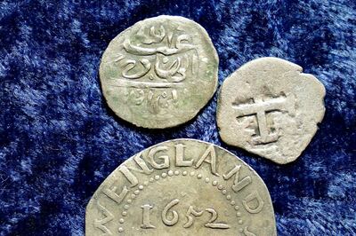 A 17th century Arabian silver coin, top, that research shows was struck in 1693 in Yemen, rests near an Oak Tree Shilling minted in 1652 by the Massachusetts Bay Colony, below, and a Spanish half real coin from 1727, right, on a table, in Warwick, R.I., Thursday, March 11, 2021. The Arabian coin was found at a farm, in Middletown, R.I., in 2014 by metal detectorist Jim Bailey, who contends it was plundered in 1695 by English pirate Henry Every from Muslim pilgrims sailing home to India after a pilgrimage to Mecca. (AP Photo/Steven Senne)