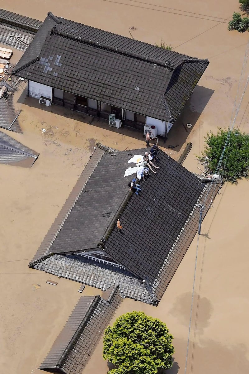 Residents are stranded on the rooftop of a house submerged in muddy waters that gushed out from the Kuma River in Hitoyoshi, Kumamoto prefecture. Kyodo News via AP