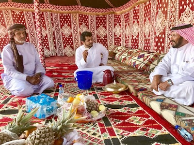 Mohammed Salem, centre, relaxes at a camp on the first morning of the Al Dhafra Festival with Saeed Al Mehri, left, and Ahmed Salem, right. Anna Zacharias / The National