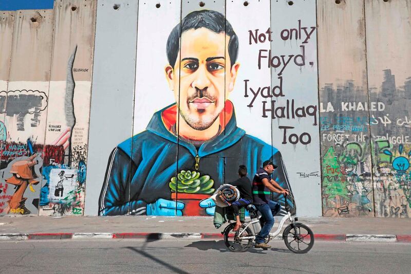 A Palestinian man rides a bike past a mural depicting Iyad Hallak, a 32-year-old autistic Palestinian man shot dead by Israeli police on a section of Israel's controversial separation barrier in Bethlehem. AFP