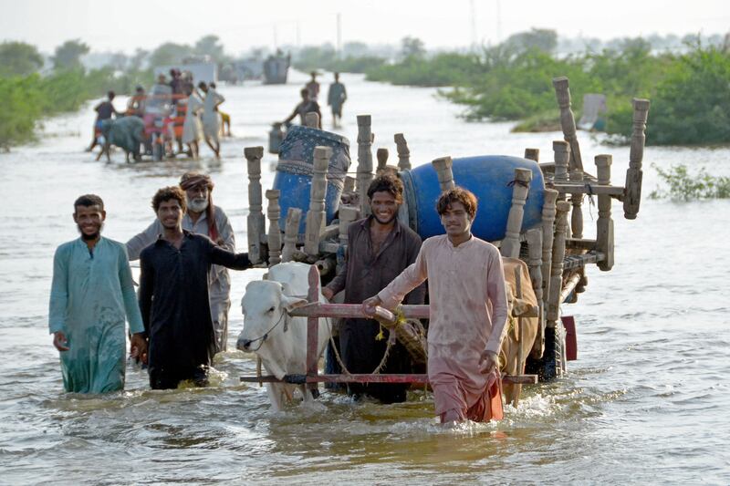 Smiling through the hardship, people who fled their homes with their belongings wade through a flooded street in the Sohbatpur area of Jaffarabad district in Balochistan. AFP