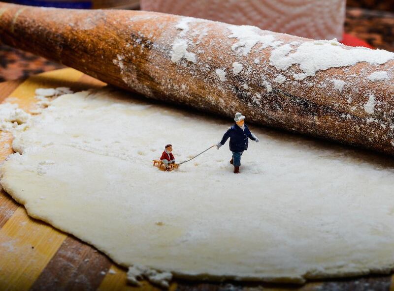 A man pulls a child on a sledge through a snow scene created by flour and pastry. The image is captioned as "In a Cheesecake Factory". Courtesy Omar Maree Humaid