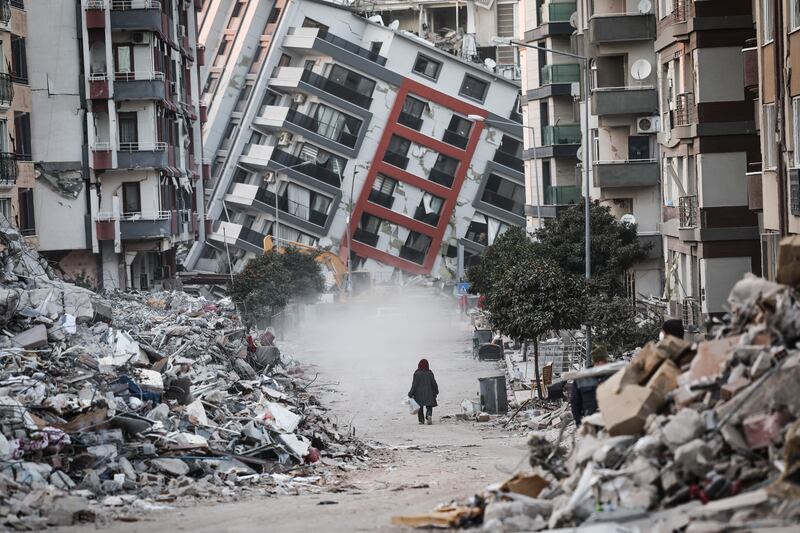 A woman walks by a collapsed building while demolition teams work after the earthquake, in Hatay, Turkey. EPA