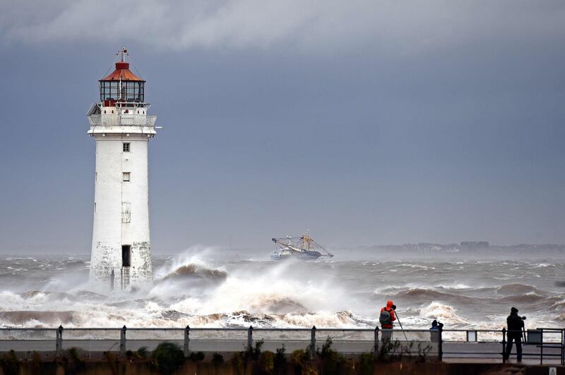 People walk along the promenade as waves in break in a stormy sea alongside the lighthouse in New Brighton, north west England as Storm Ciara swept over the country.   AFP