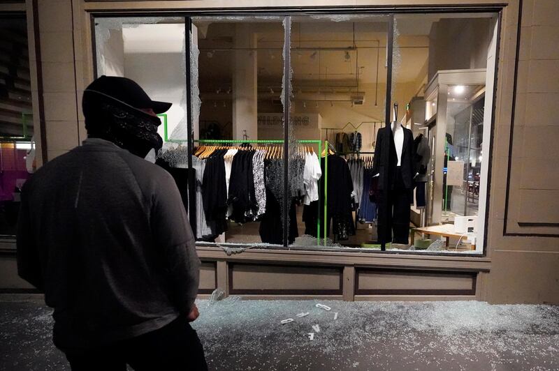 A man stands in front of a broken display window at a retail store during protests in Portland, Oregon. AP Photo