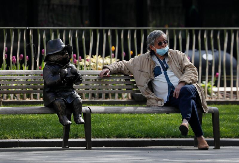 A man relaxes on a bench in London, next to a sculpture of Paddington Bear, as the country is in lockdown to help curb the spread of the coronavirus. AP Photo