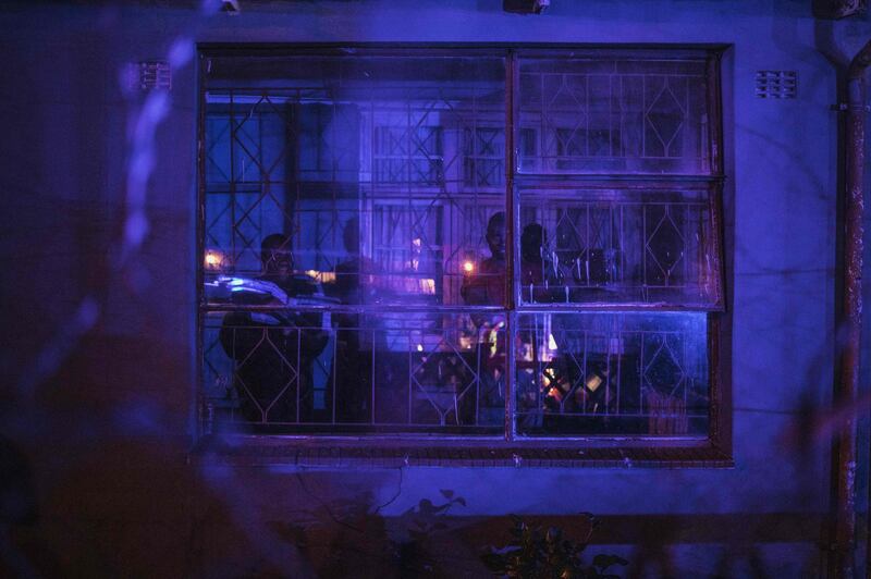 A family look from inside their residence as South African police officers converge on the site of an incident involving a police officer during a lockdown in Johannesburg. Police forces are out in large numbers on the streets of Johannesburg to ensure that the lockdown is respected. AFP