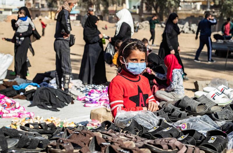 A girl wearing a protective mask amid the COVID-19 pandemic sells slippers at an open-air market in the city of Raqa in east central Syria on February 24, 2021. After a decade of unfathomable violence and human tragedy that has made Syria the defining war of the early 21st century, the fighting has tapered off but the suffering hasn't. / AFP / Delil SOULEIMAN
