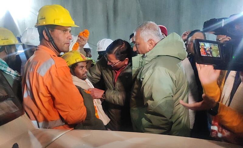 Uttarakhand Chief Minister Pushkar Singh Dhami, centre,  and Union Minister VK Singh, right, give a garland to a rescued worker who had been trapped inside a tunnel in Uttarkashi, India. AFP