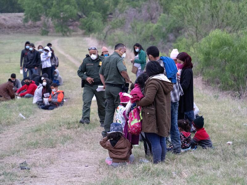 A group of 60 migrants weight in a field as US Border Patrol agents inspect their documents and belongings. Willy Lowry/ The National
