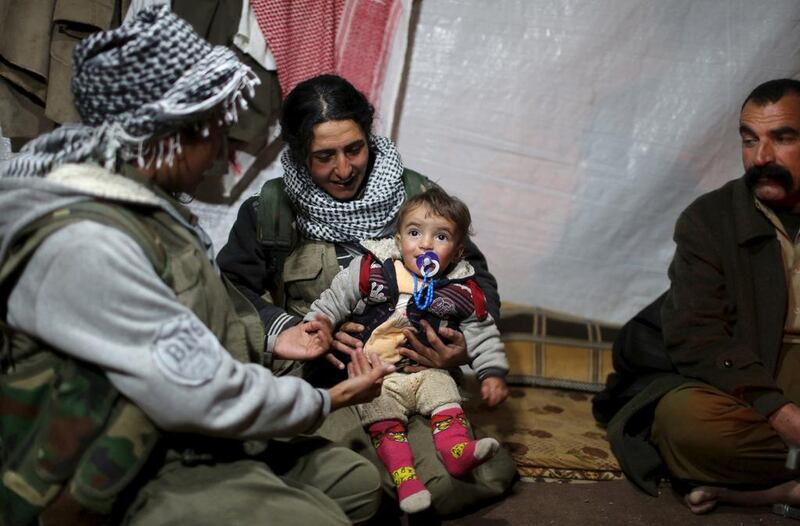 A PKK fighter sits with a Yazidi family, including a member of YBS Yazidi militant group, near their base in Sinjar.  Asmaa Waguih / Reuters