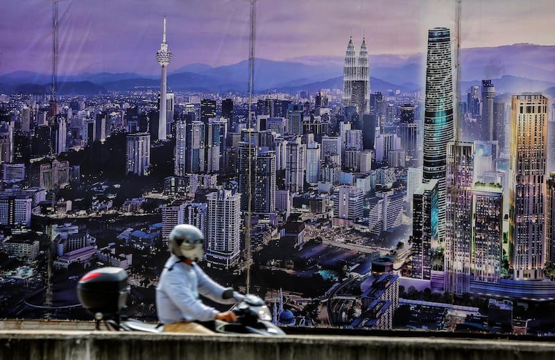 epa06426200 A motorist drives his vehicle in front nof a poster showing the capital Kuala Lumpur's future city skyline at twilight, in Kuala Lumpur, Malaysia, 09 January 2018. Malaysia's gross domestic product (GDP) is expected to grow about five percent in 2018. Malaysia's gross domestic product (GDP) is expected to grow around five percent in 2018.  EPA/AHMAD YUSNI