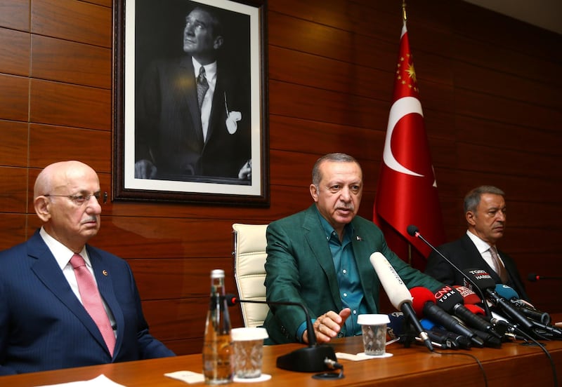 Turkey's President Recep Tayyip Erdogan, center, speaks to the media at Ataturk Airport before his departure for London for a two-day official visit, in Istanbul, Sunday, May 13, 2018. Parliament Speaker Ismail Kahraman, left, and Chief of Staff Gen. Hulusi Akar listen.(Presidential Press Service/Pool via AP)