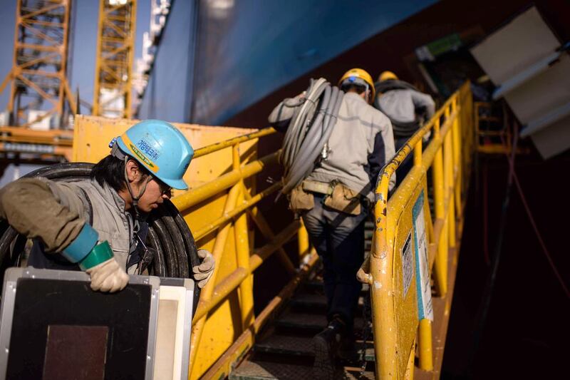 Workers carry materials as they enter an under-construction Maersk triple-E class container ship at the Daewoo DSME shipyard. Ed Jones / AFP