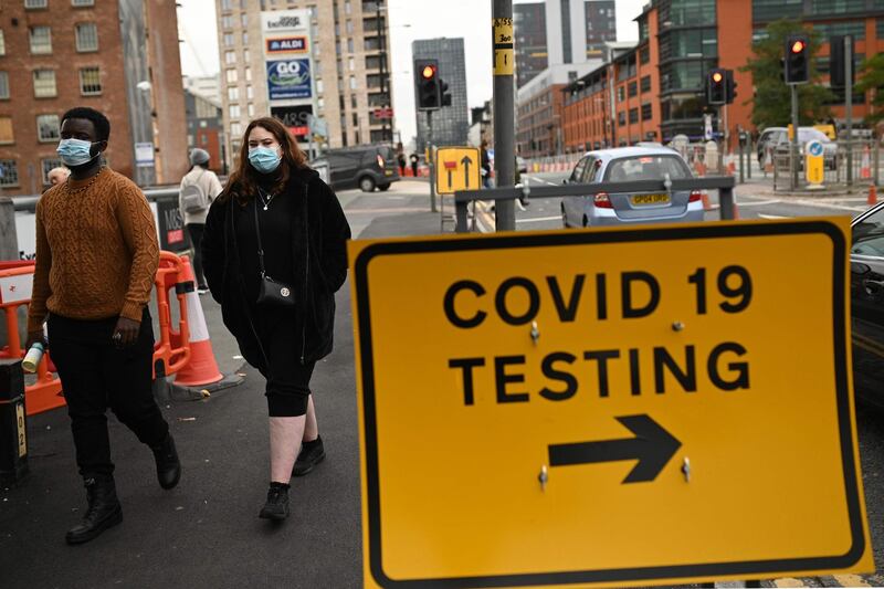 Pedestrians wearing protective face coverings walk past a Covid-19 testing sign in Manchester. AFP