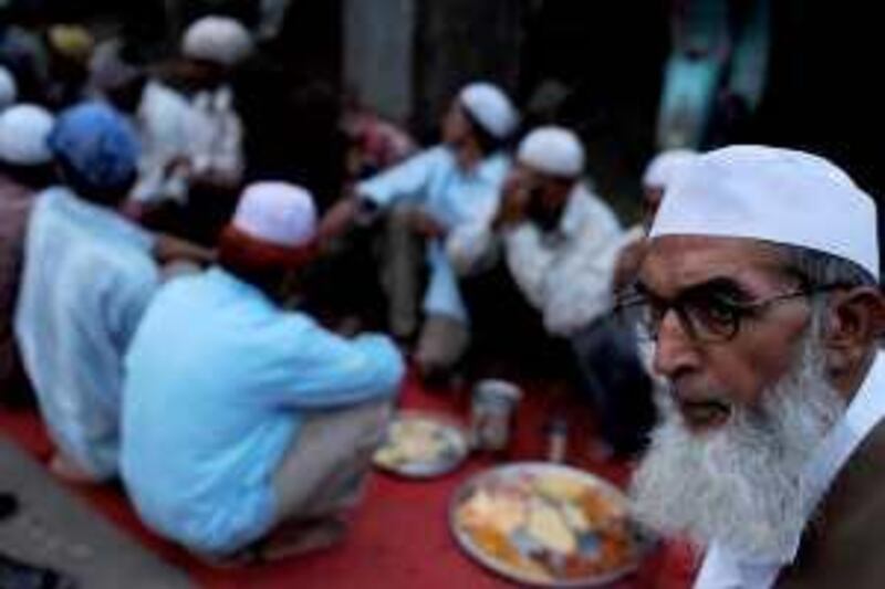 An Indian Muslim man looks on as mechanics pray prior to breaking fast during the holy month of Ramadan outside the garage in Allahabad on September 2, 2009.  During Ramadan, Muslims are required to abstain from food, drink and sex from dawn to dusk as life slips into a lower gear during the day. Activity peaks between 'iftar', the breaking of the fast at sunset, and 'suhur', the last meal of the day before sunrise.   AFP PHOTO/Diptendu DUTTA *** Local Caption ***  713469-01-08.jpg