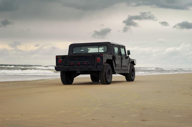 Noordwijk, The Netherlands - June 19, 2004: Two people in a black Hummer H1 SUV are driving on a beach on a cloudy day.