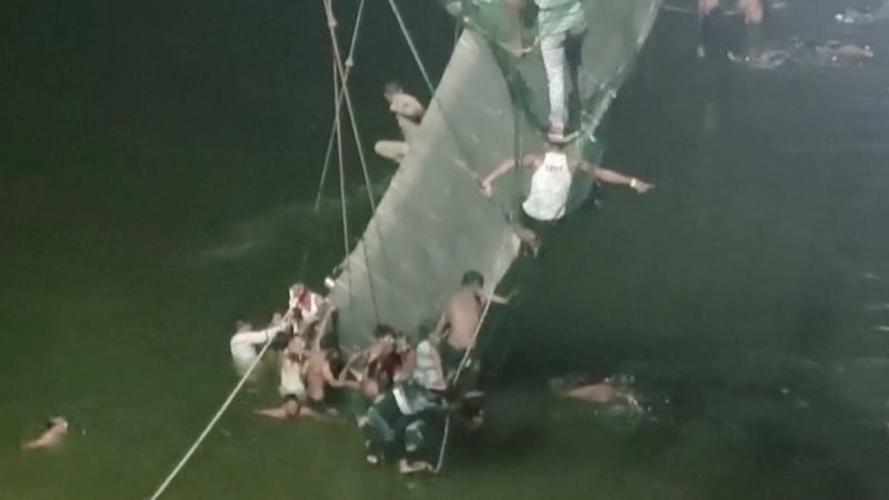 People cling on to the collapsed suspension bridge in Morbi, Gujarat state. Reuters