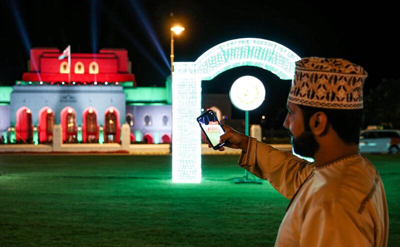 An Omani uses his phone to take a picture as he stands on the lawn before the Royal Opera House Muscat in Oman's capital, lit up with the national colours on the occasion of the Omani national day.  AFP