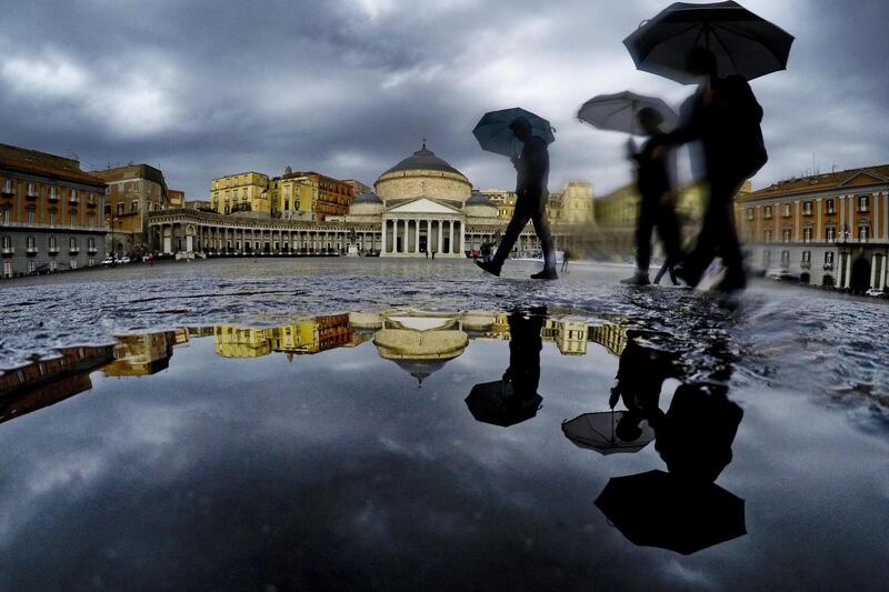 Pedestrians are reflected in a puddle in central Naples, southern Italy. EPA