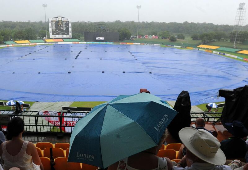 Cricket fans shelter from the rain as match is stopped due to the rain during the first one day international (ODI) cricket match between Sri Lanka and England at the Rangiri Dambulla International Cricket Stadium in Dambulla on October 10, 2018. / AFP / LAKRUWAN WANNIARACHCHI
