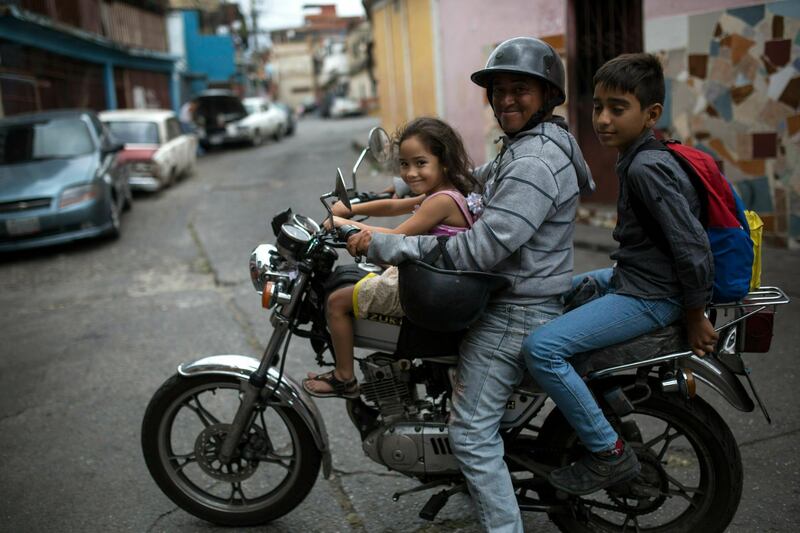 A man strikes a pose while driving a motorcycle with his children as passengers in the 23 de Enero neighborhood, Caracas, Venezuela, Friday, May 3, 2019. (AP Photo/Rodrigo Abd)