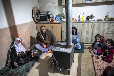Jaber Abu Queder 51,  head of local council of the unrecognised village of Al-Zarnoug with his family as they sit on their kitchen floor around a wood stove to keep warm  in the early evening. The village is not connected to the electricity grid and power is supplied mostly through solar panels .(Photo by Heidi Levine for The National).