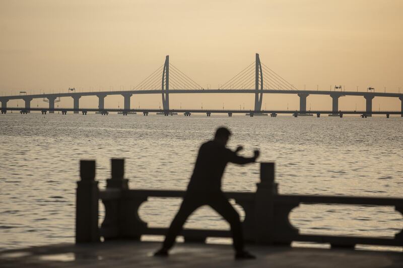 A man exercises along a promenade as a section of the Hong Kong-Zhuhai-Macau Bridge, rear, stands in the background in Zhuhai, China, on Monday, Oct. 22, 2018. The $15 billion, 55-kilometer (34-mile) bridge, which Xinhua News Agency says is the world’s longest sea link, opens for business on Wednesday. Photographer: Qilai Shen/Bloomberg