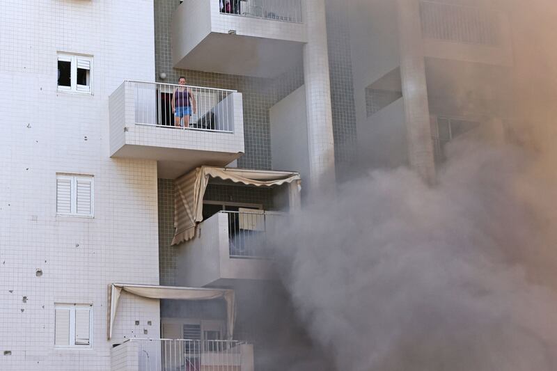 A woman stands on her balcony as smoke billows in the parking lot of a residential building following an attack from the Gaza Strip. AFP