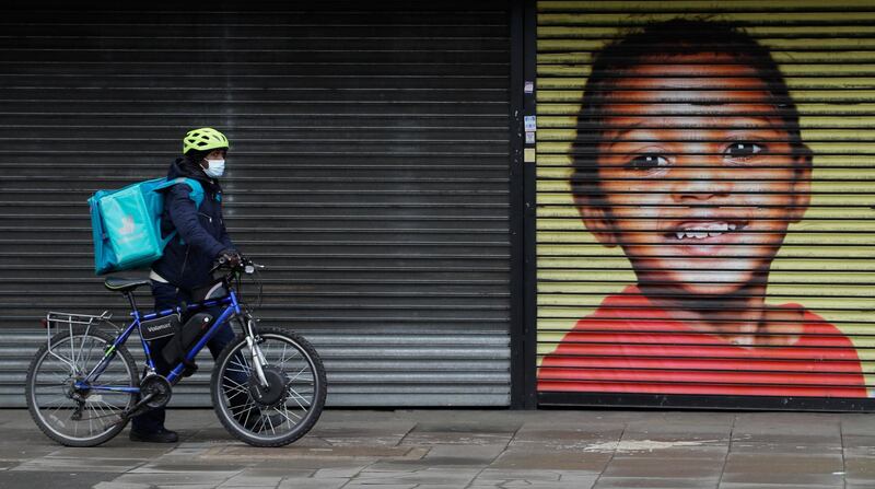 A food delivery rider passes the shutters of a closed shop in West Ealing in London. AP Photo
